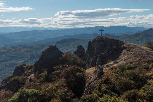 View from Azeula Fortress across the Trialeti ridges — iron cross on rock, mountain ranges to the horizon
