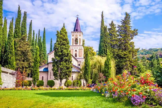 Bell tower of Bodbe Monastery rising above cypress trees and flower gardens, Sighnaghi, Kakheti