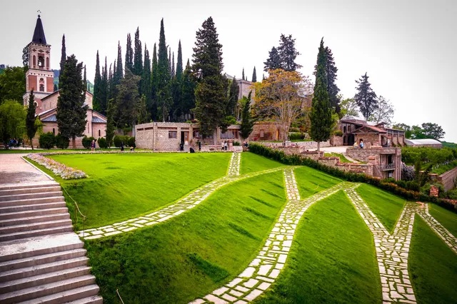 Aerial view of Bodbe Monastery grounds with stone pathways crossing green lawns, bell tower and monastery buildings among cypress trees, Kakheti Georgia