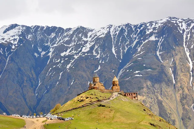 Gergeti Trinity Church viewed from below with parking area and visitors visible, Stepantsminda, Georgia