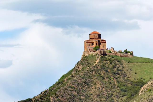 Jvari Monastery on a hilltop viewed from below, green slopes and dramatic cloudy sky