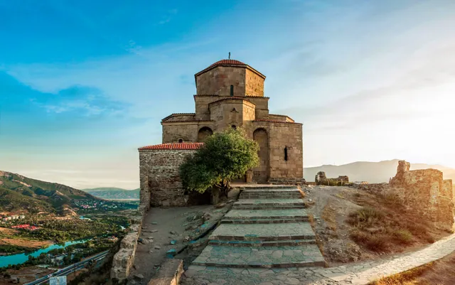 Jvari Monastery at golden hour, stone steps leading to the entrance, river valley visible below