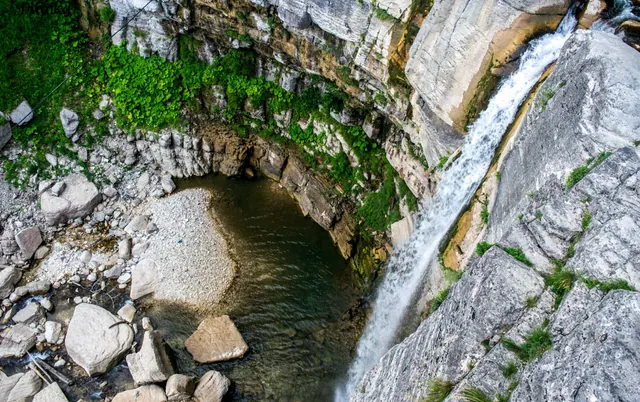 Bird's-eye view into the base pool of Kinchha Waterfall — stream, green moss, and rocky pool