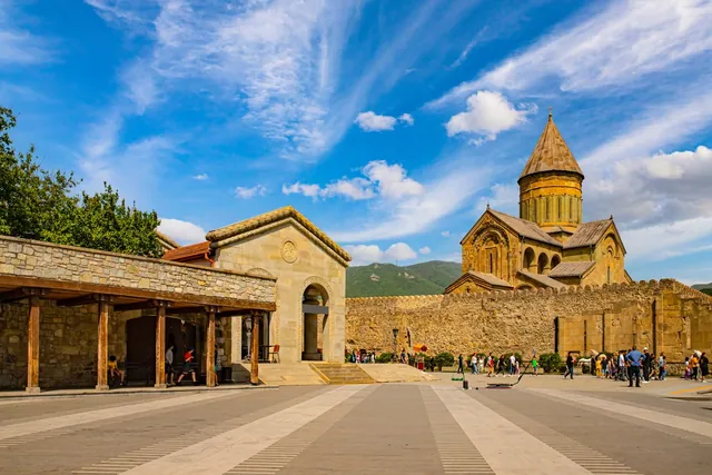 The plaza at Svetitskhoveli Cathedral in Mtskheta — fortress walls, arched gate and tourists on a sunny day