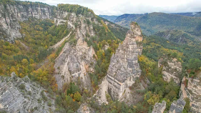 Sairme Pillars in autumn — two tall rock towers against golden and green forest foliage, mountain ranges behind, Georgia