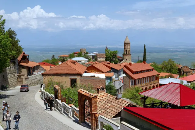 Cobbled street in Sighnaghi with a red Lada and the bell tower of St George's Church above the valley