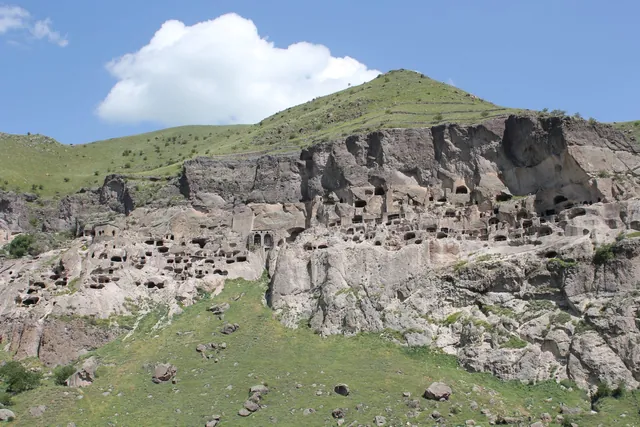 The cave city of Vardzia in the cliff above a green slope